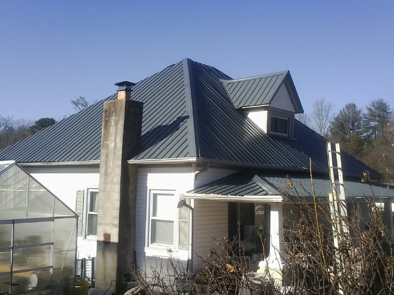 Dark blue standing seam metal roof on a white farmhouse with dormer — Slate & Tile Roof Repair by Roofing Brothers in Welton