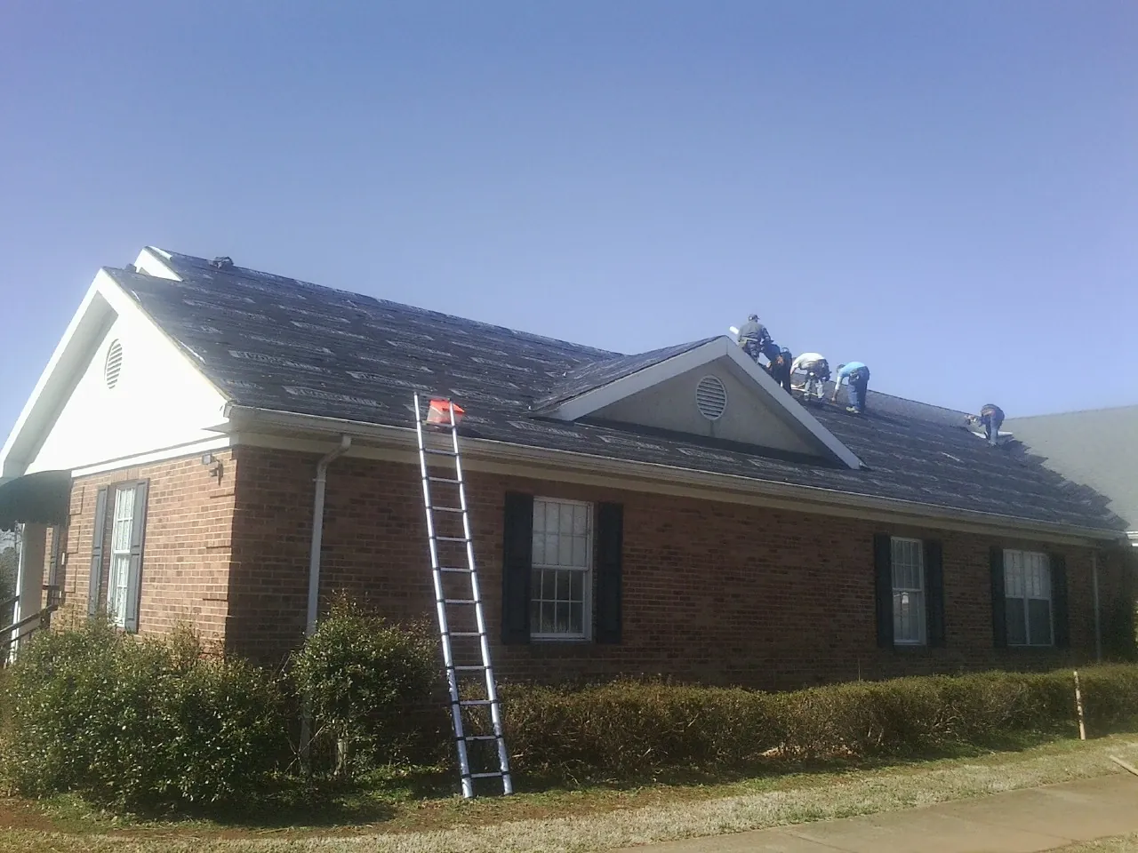 Crew tearing shingles off a brick ranch roof with a ladder set — Emergency Roof Repair work by our crew in Welton