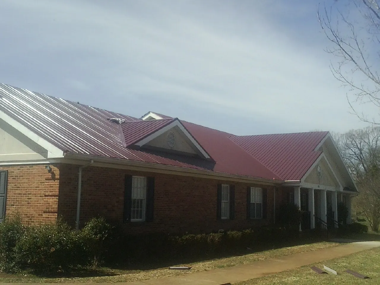 Red metal roof with gabled entries on a long brick building, from a Hail Damage Roof Repair job in Welton
