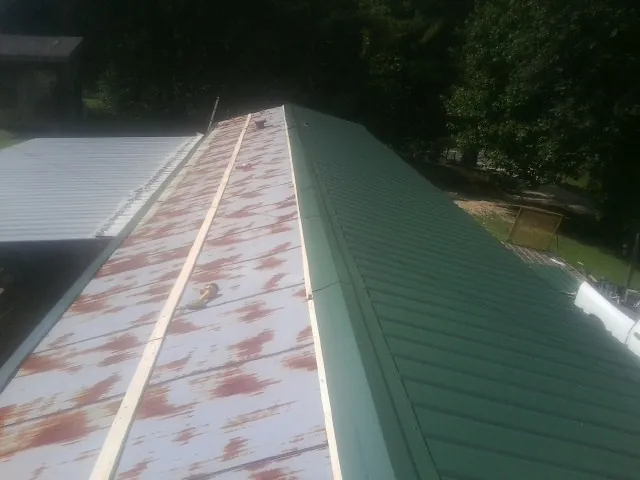 Old rusted panels beside newly installed green metal roofing — Wind Damage Roof Repair by Roofing Brothers in Welton