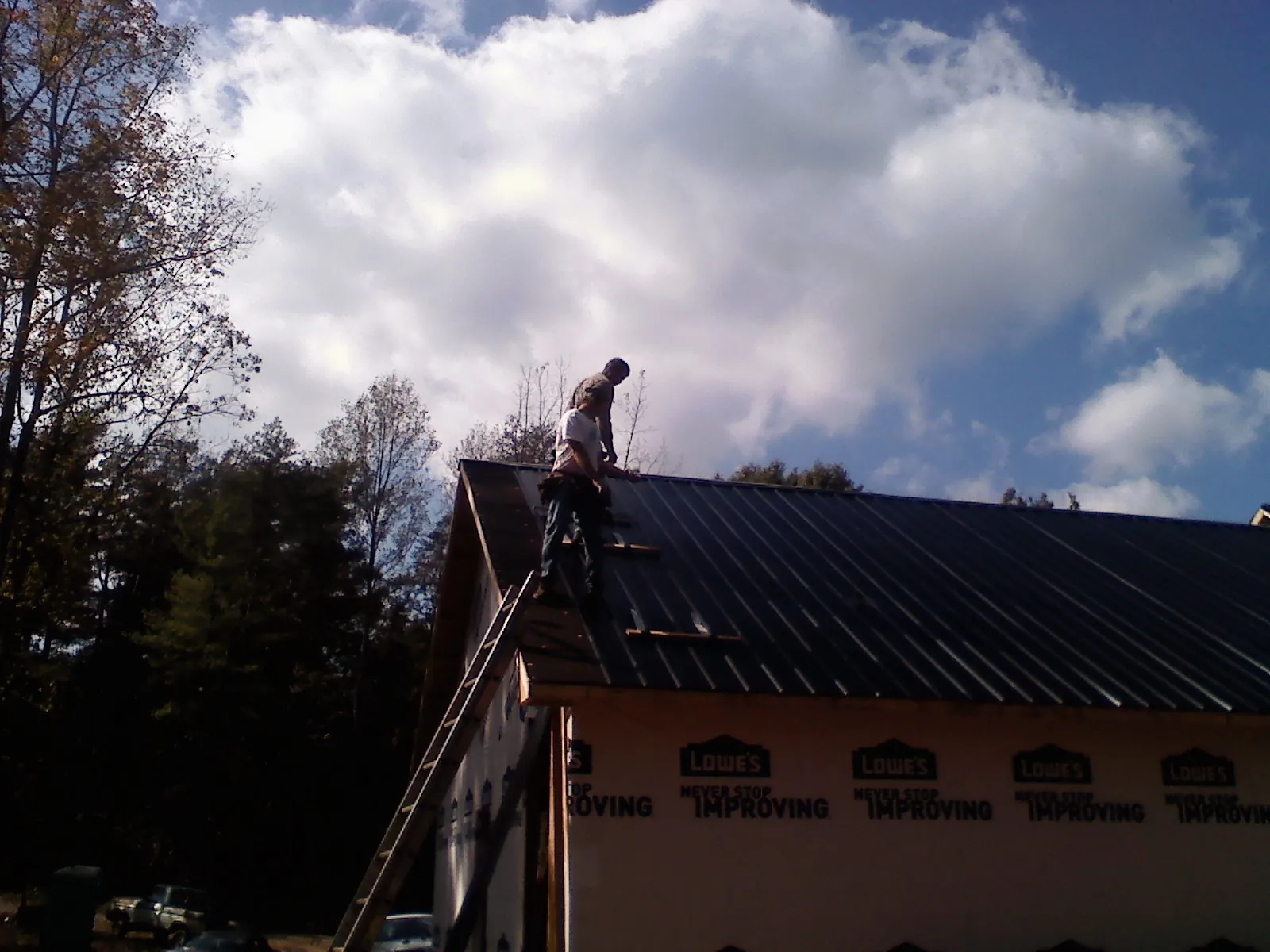 Roofer fastening dark metal panels high against a cloudy sky, from a Roof Inspection job in Welton
