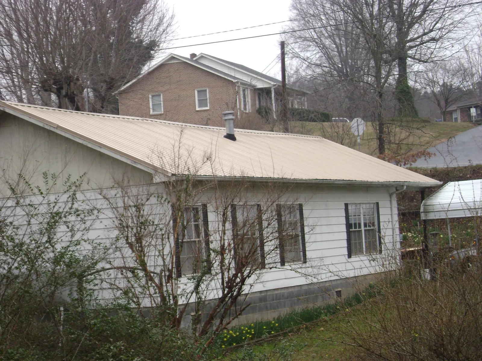 Tan metal roof on a white sided house set into a hillside — Commercial Roofing by Roofing Brothers in Welton