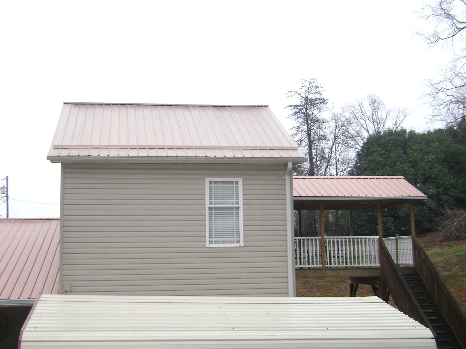 Tan metal roofs on a two story addition and attached porch, from a Roof Replacement job in Welton